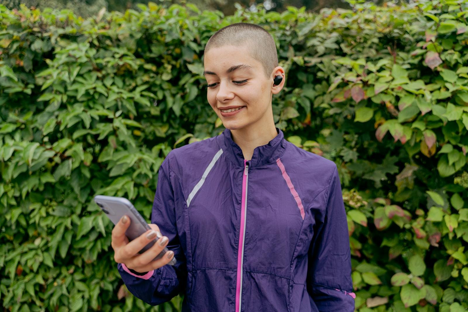 Smiling woman in athletic wear using a smartphone outdoors enjoying nature.